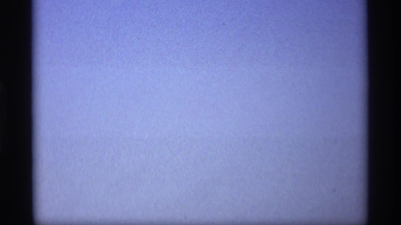 A soft, blue-tinted 8mm frame with little visible detail beyond sky or exposure wash and dark gate borders.