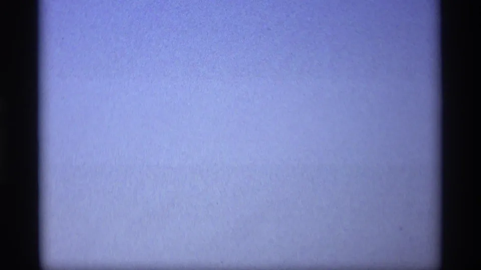 A soft, blue-tinted 8mm frame with little visible detail beyond sky or exposure wash and dark gate borders.