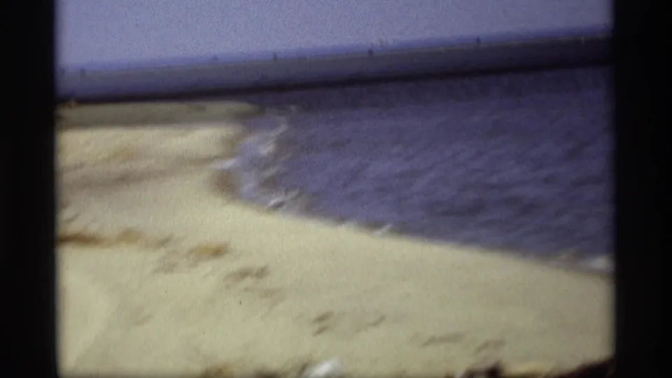 Holland, Michigan lakeshore footage shows pale sand, blue water, and a small shoreline curve in a soft 8mm frame.