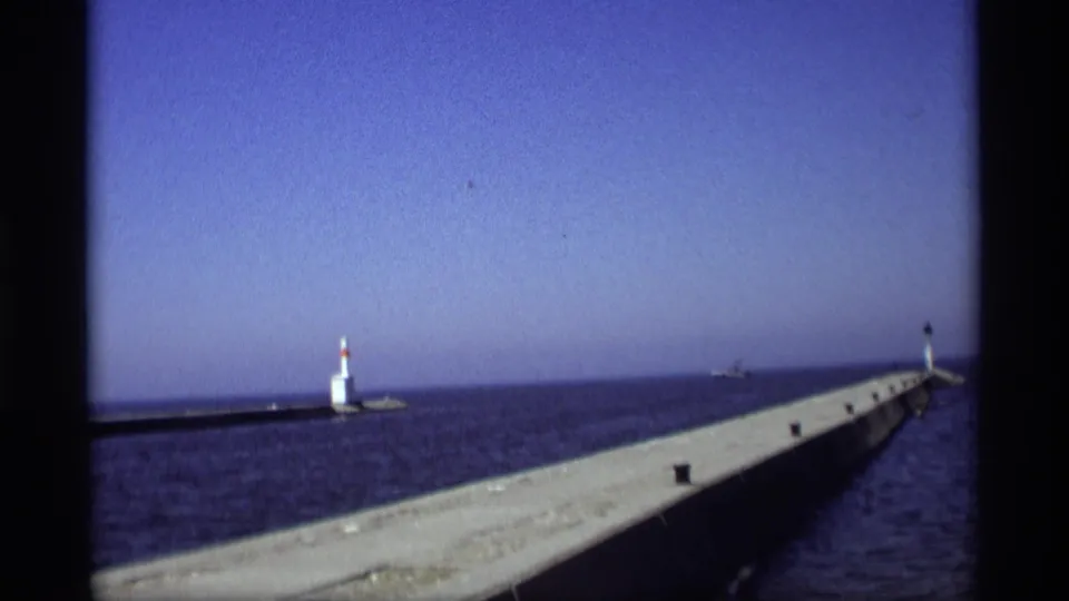 1969 Holland, Michigan frame of a long concrete pier extending into Lake Michigan toward a small lighthouse.