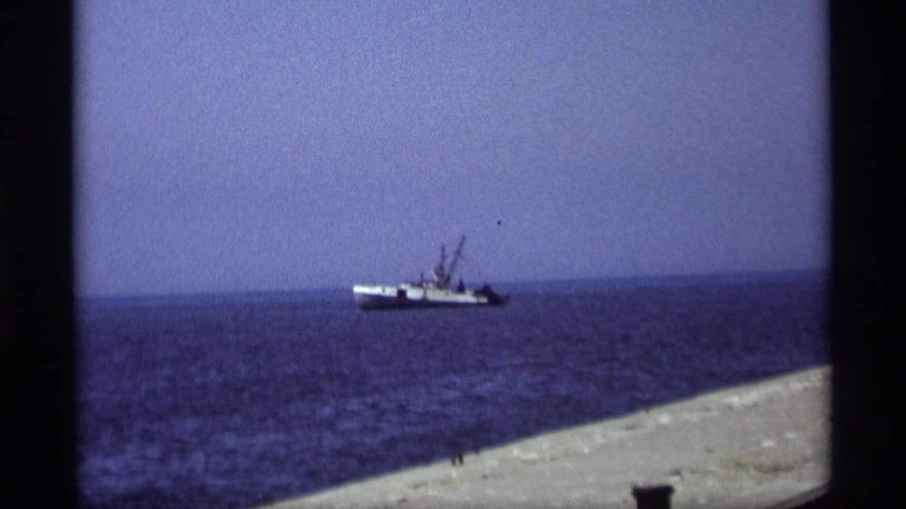 1969 Holland, Michigan 8mm frame showing a distant working boat on open water, viewed from a pier or shoreline.