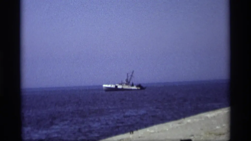 Distant boat off the Holland, Michigan shoreline, framed through soft 8mm color and a slanted pier edge.