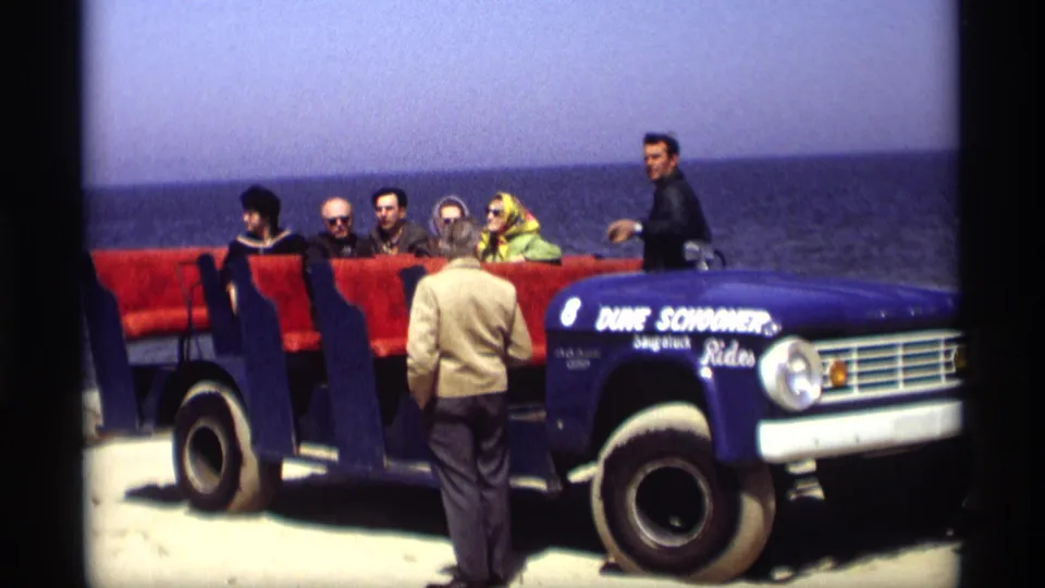 People ride or wait in a blue open-air tour vehicle near the Holland, Michigan waterfront in 1969 footage.