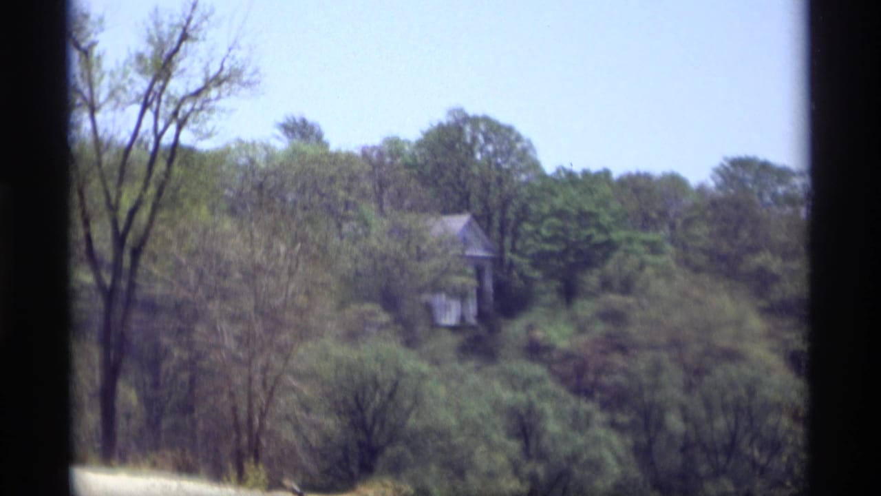 Distant white house partly hidden among trees on a wooded hillside.