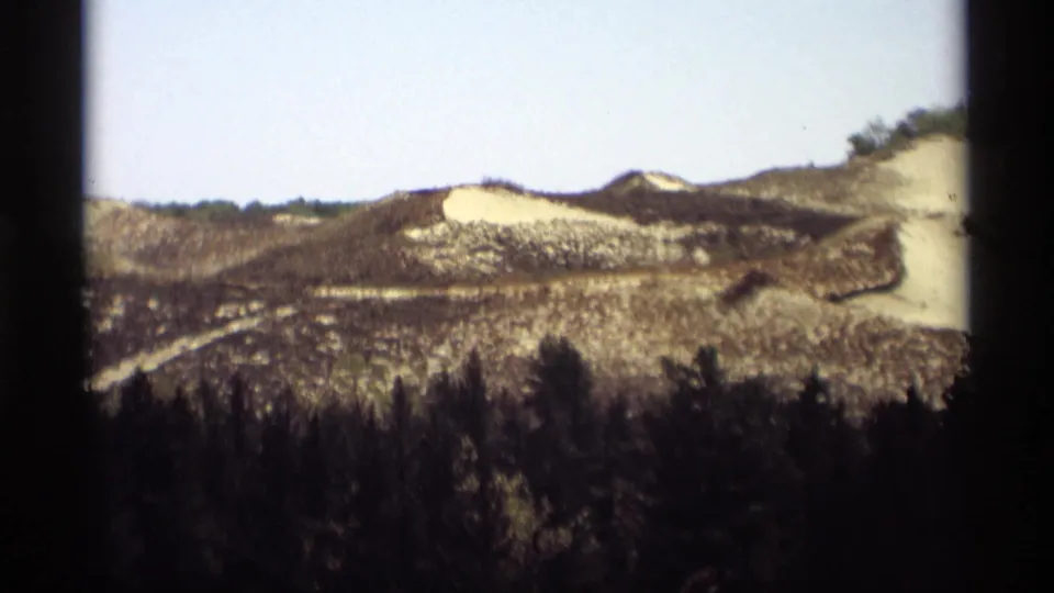 1969 Holland, Michigan 8mm frame with a wider view of blackened low hills, pale sandy patches, and dark foreground woods.
