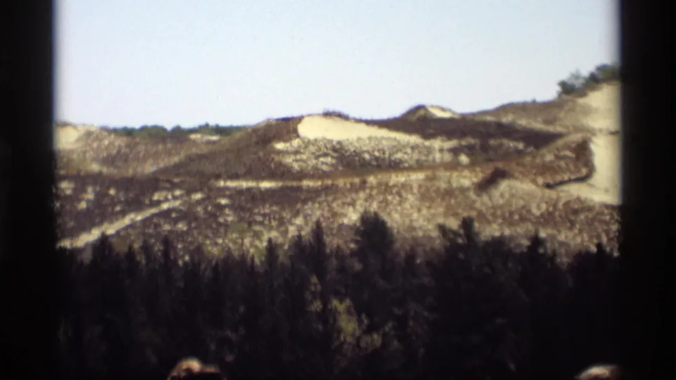 1969 Holland, Michigan home-movie view of scorched low hills and forest, with a small indistinct person partially visible at the lower edge.