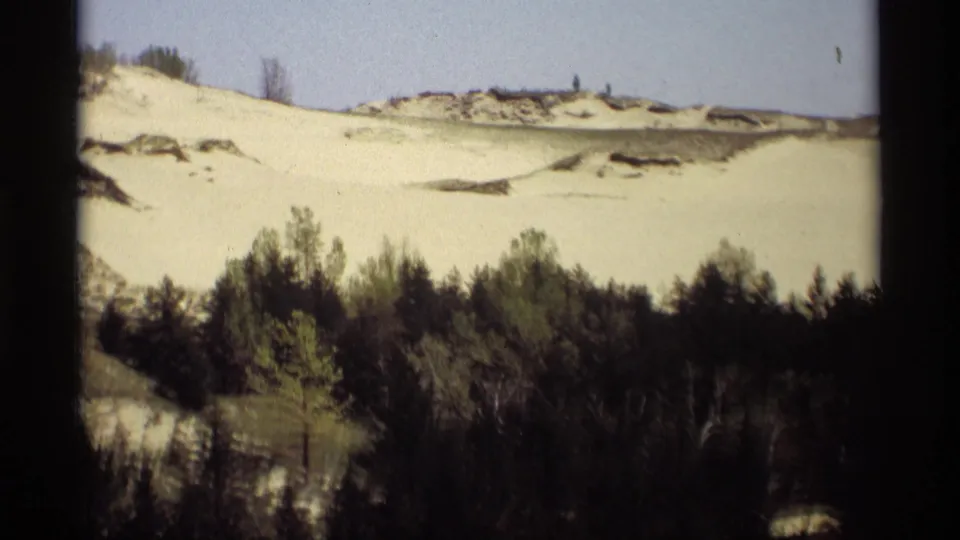 1969 Holland, Michigan dune landscape with pale snow, wooded foreground, and possible distant people on the ridge.