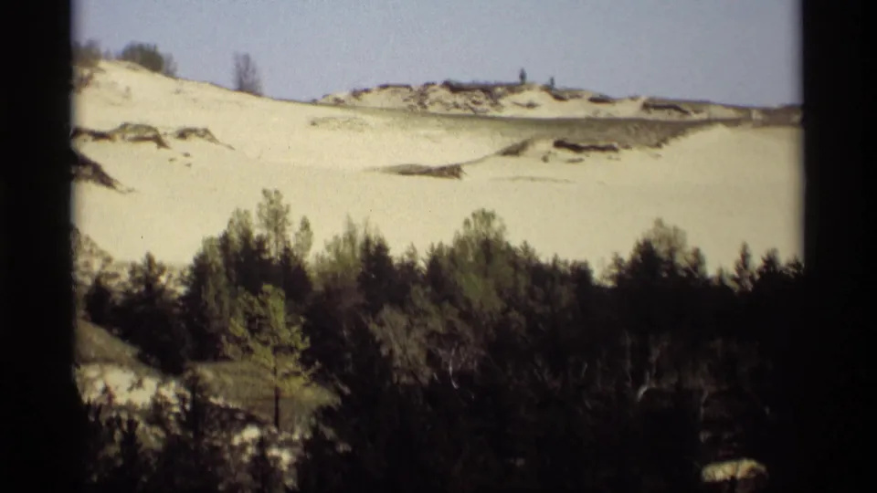 1969 8mm Holland, Michigan frame with snow-covered dunes behind a dense winter tree line.