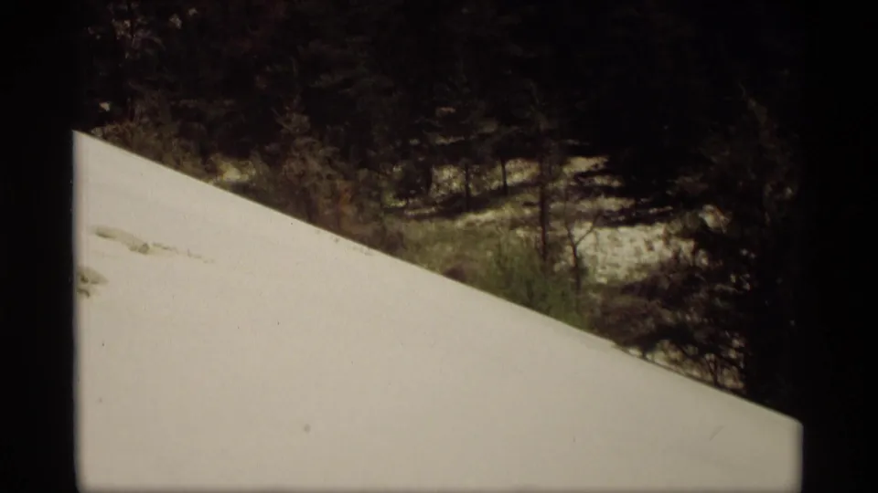 1969 Holland, Michigan 8mm frame showing the snowbank edge, a dark wooded area, and patchy snow in the background.