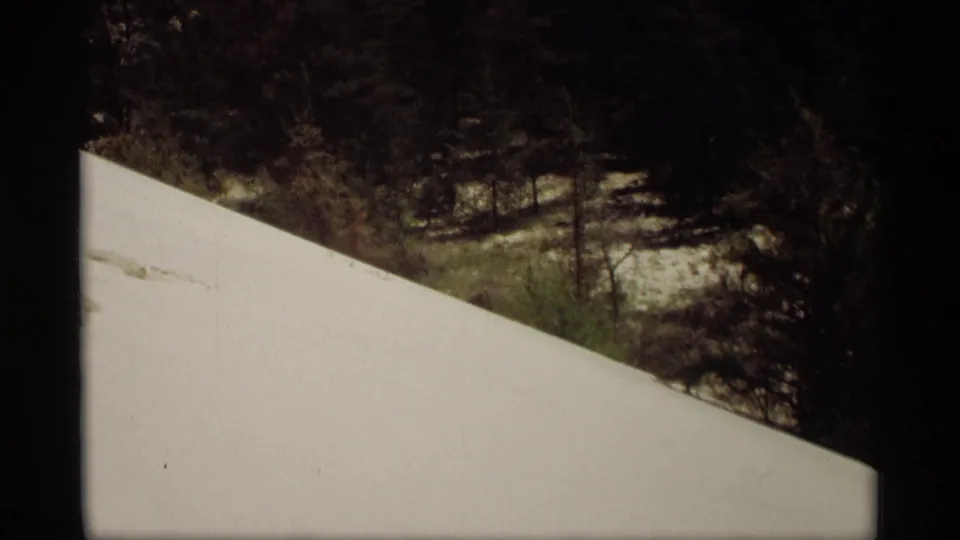 1969 Holland, Michigan home-movie frame of a smooth snowbank foreground with trees and patchy winter ground beyond.