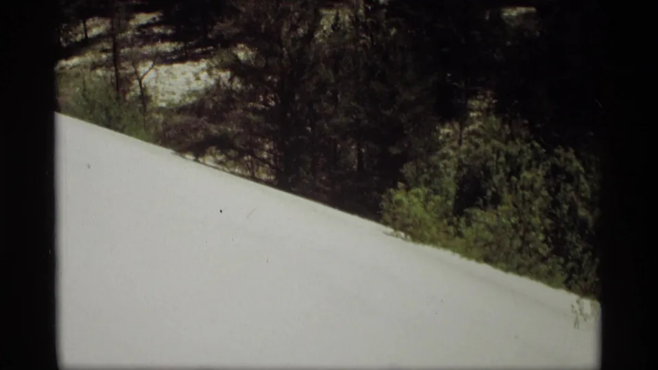 1969 Holland, Michigan 8mm frame showing a sloped snow field with evergreens and brush behind it.
