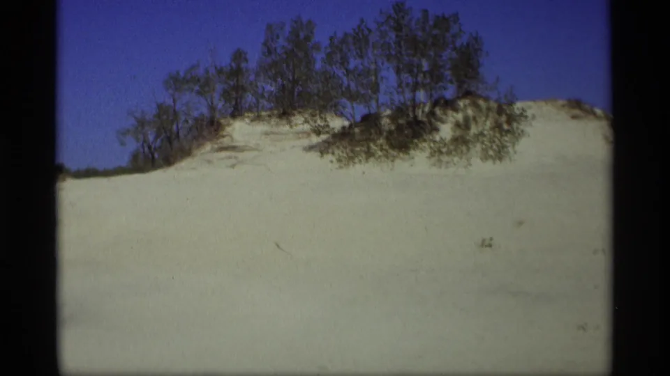 1969 Holland, Michigan 8mm frame showing a wide snow slope, tree-topped ridge, and blue sky.