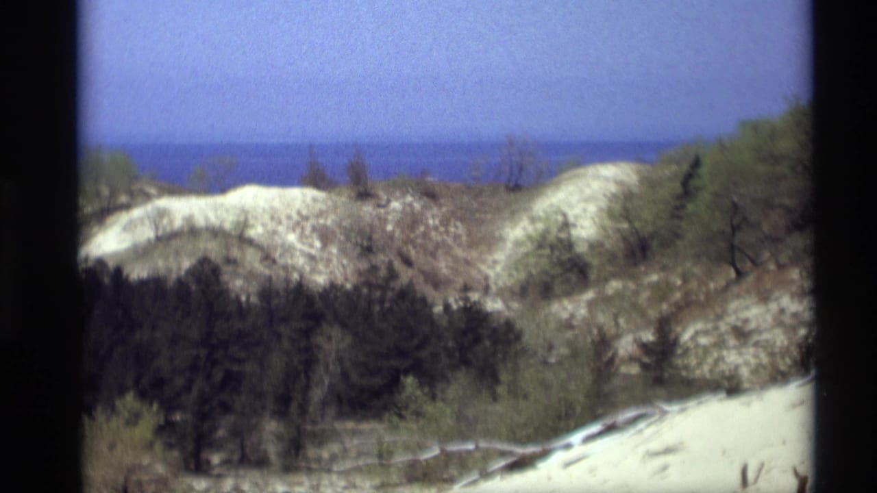 1969 8mm home-movie view from Holland, Michigan, showing pale dunes, sparse vegetation, and distant lake water.