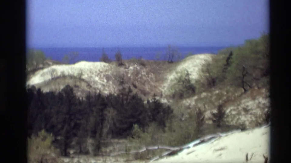 1969 8mm home-movie view from Holland, Michigan, showing pale dunes, sparse vegetation, and distant lake water.