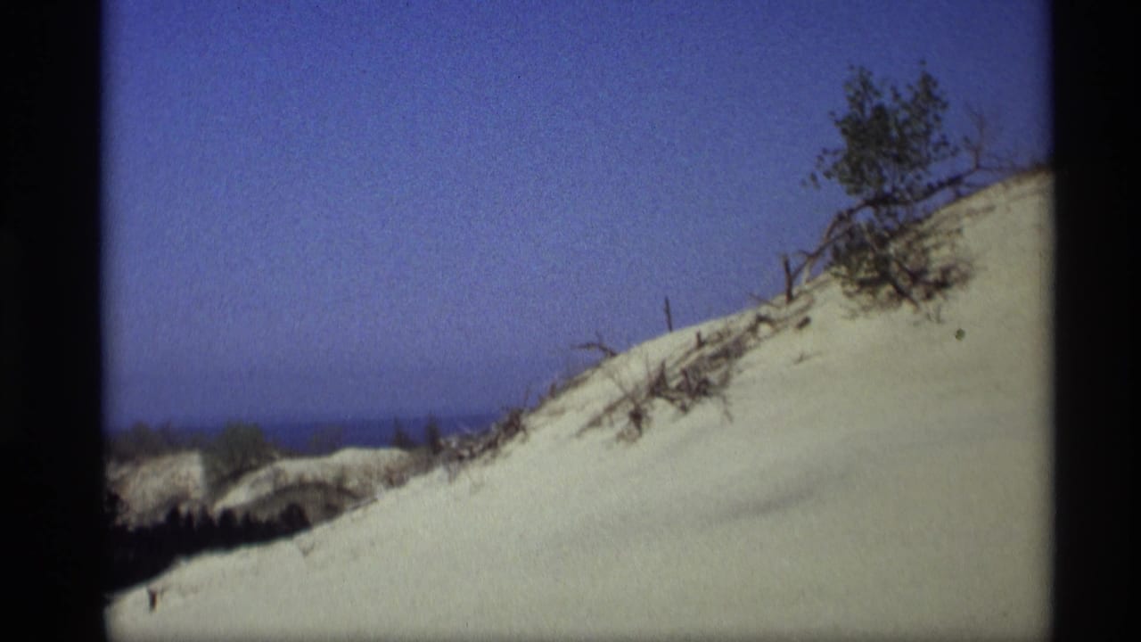 Holland, Michigan dune slope on 8mm film, with scattered brush, a clear sky, and the lake visible near the horizon.