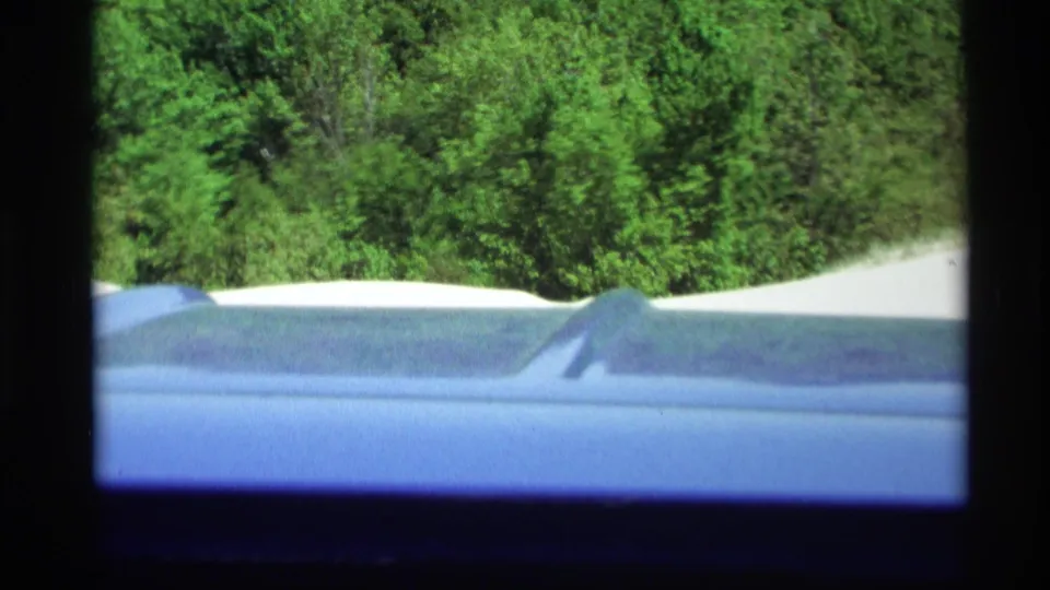 End frame from a 1969 Holland, Michigan home movie showing part of a parked car near trees and sand dunes.