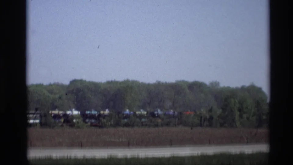 A roadside view in 1969 Holland, Michigan shows a distant freight train beside trees beyond the highway.
