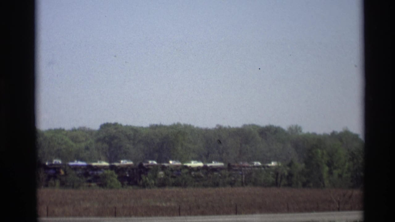 Distant freight train and road seen through a dark window frame across a brown field.