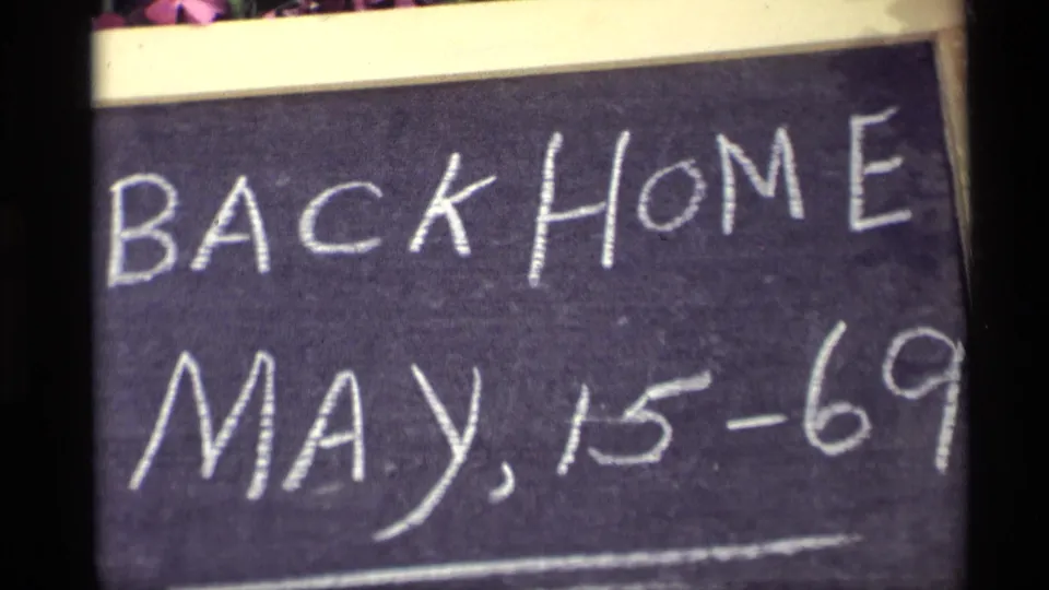 Close 1969 8mm frame of a handwritten Back Home May 15-69 chalkboard sign in Holland, Michigan.