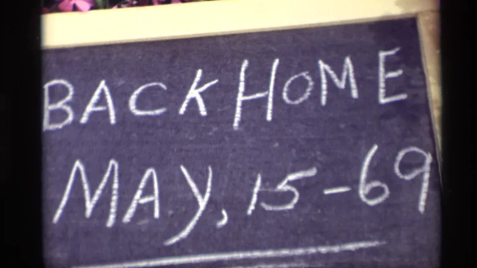Handwritten Back Home May 15-69 sign fills the frame in 1969 Holland, Michigan home-movie footage.