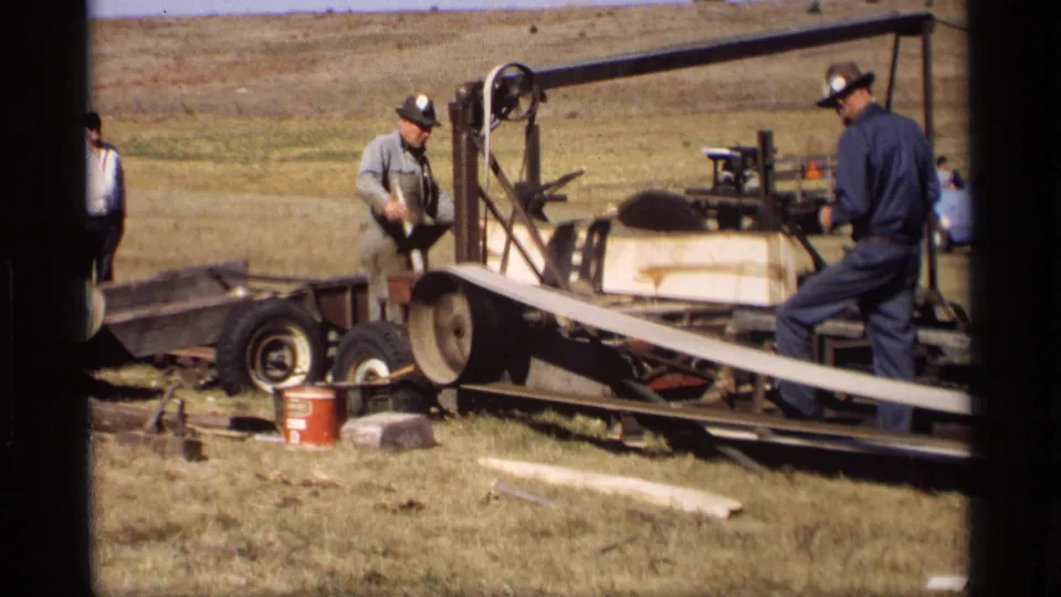 A worker in Jordan, Minnesota appears to operate or monitor a portable band saw as a wooden slat crosses the frame in 1969 home-movie footage.