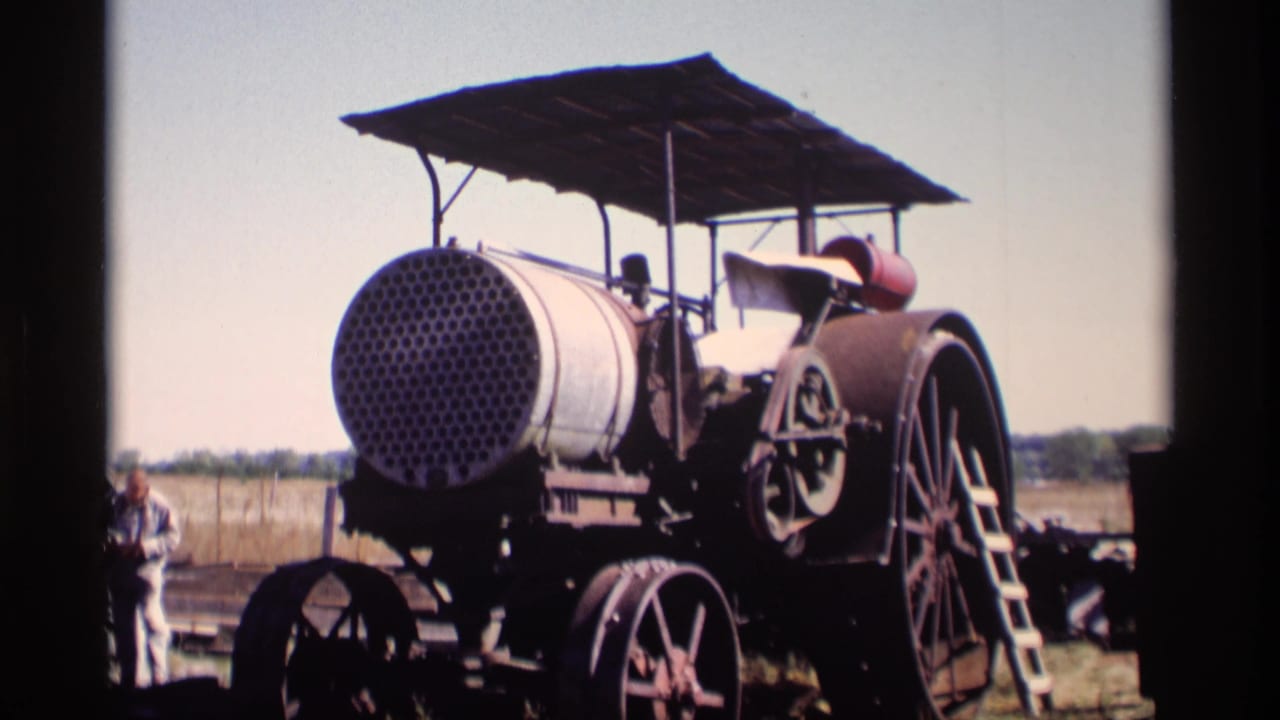 1969 Jordan, Minnesota 8mm frame of a weathered steam traction engine with perforated boiler front, canopy, spoked wheels, and a nearby adult bystander.