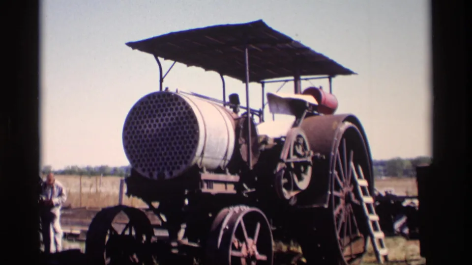 1969 Jordan, Minnesota 8mm frame of a weathered steam traction engine with perforated boiler front, canopy, spoked wheels, and a nearby adult bystander.
