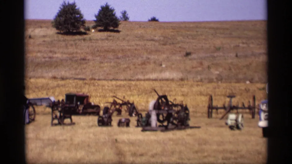 1969 Jordan, Minnesota home-movie frame showing antique buggies, carriages, and farm equipment arranged across a dry rural field.