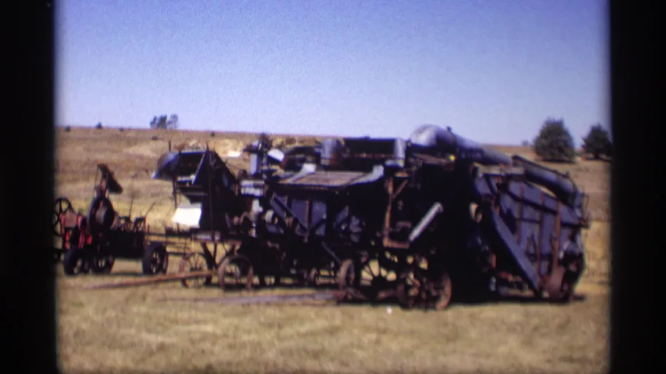 A blue vintage agricultural machine sits in a sunlit Minnesota field with additional farm equipment visible nearby.