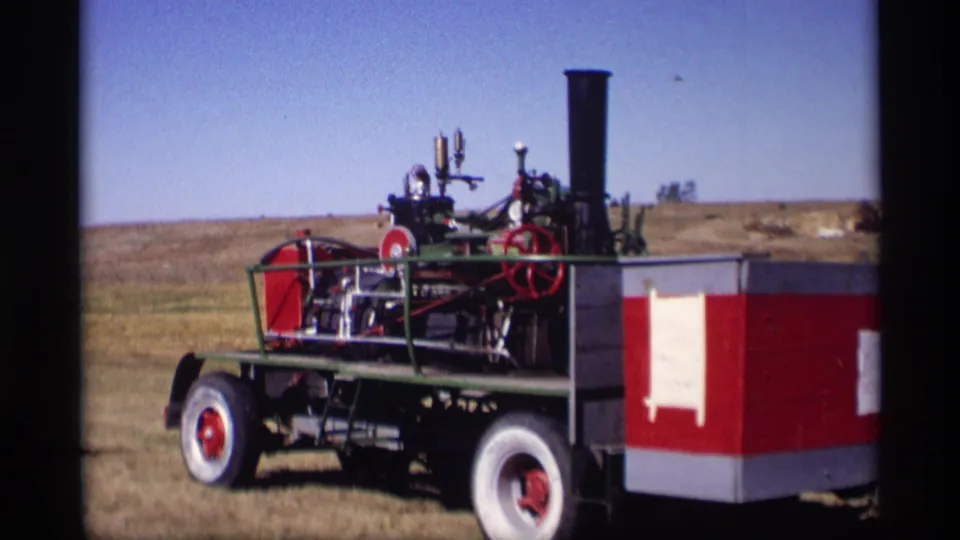 Side view of the red and white steam tractor in a sunlit Jordan, Minnesota field in 1969 footage.
