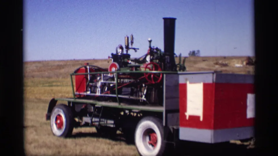 1969 home-movie frame showing the steam tractor's side, smokestack, red wheels, and white rear body panel.