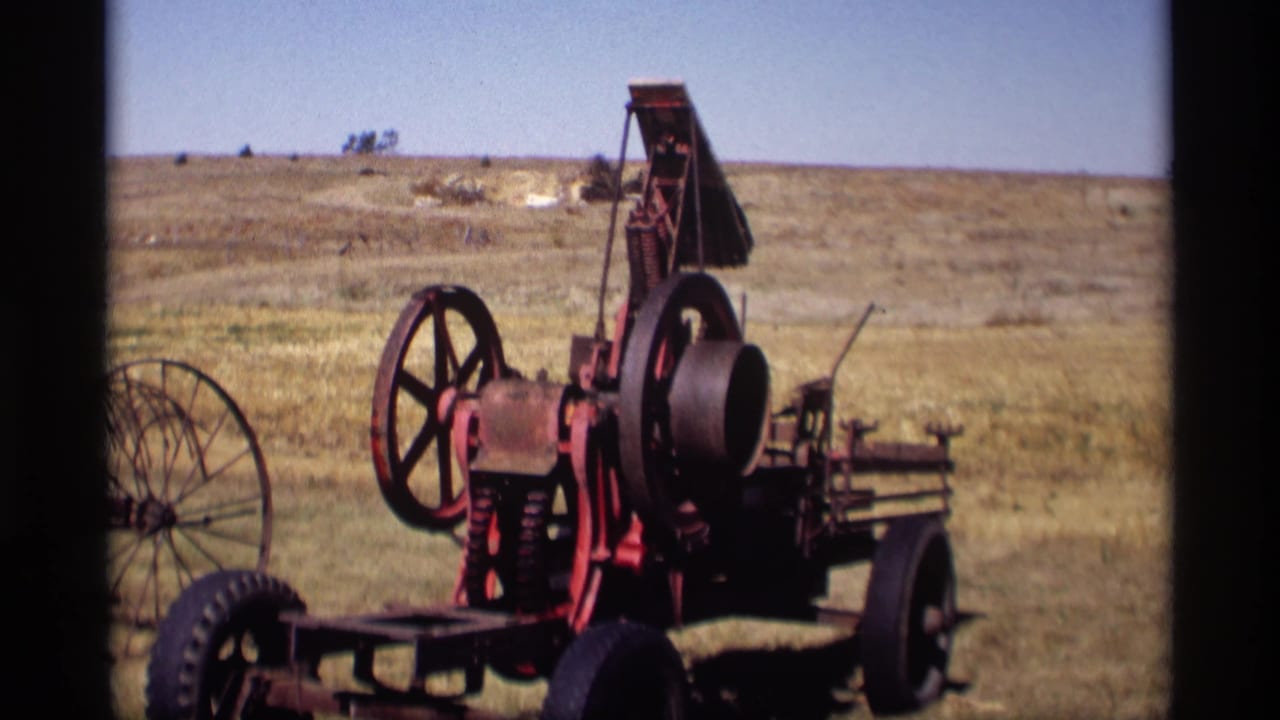 Red wheeled farm engine standing in a dry grassy pasture under a clear sky.
