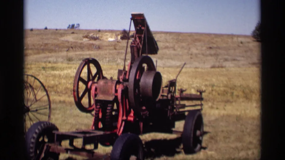 1969 Jordan, Minnesota home-movie frame of a red wheeled farm engine viewed across dry grass, with open rural land in the background.