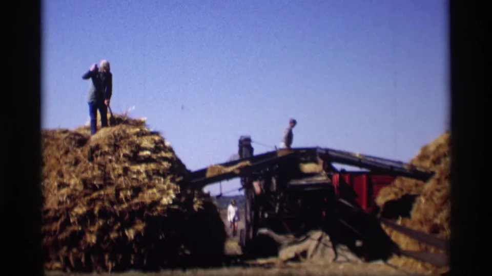 Farm workers handle hay around a wagon in the supplied rural Minnesota home-movie footage, with stacked hay and clear sky dominating the frame.
