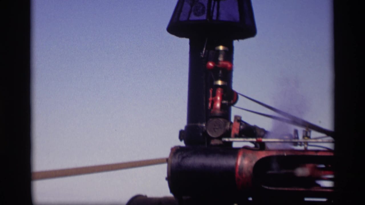 Close view of a black and red farm engine or machinery component against a pale sky.