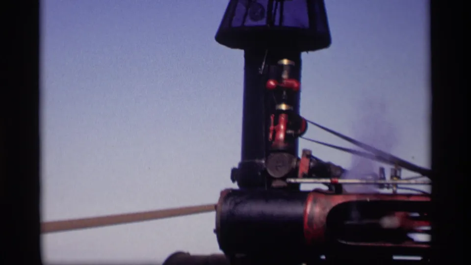 Close-up of black and red agricultural machinery in the 1969 Jordan, Minnesota home-movie clip, with soft focus and pale sky behind it.
