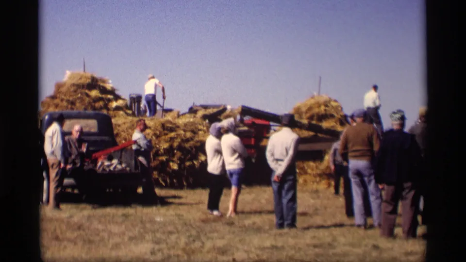 Wide 1969 Jordan, Minnesota farm scene with adults watching workers around hay piles, a pickup truck, and harvest equipment.