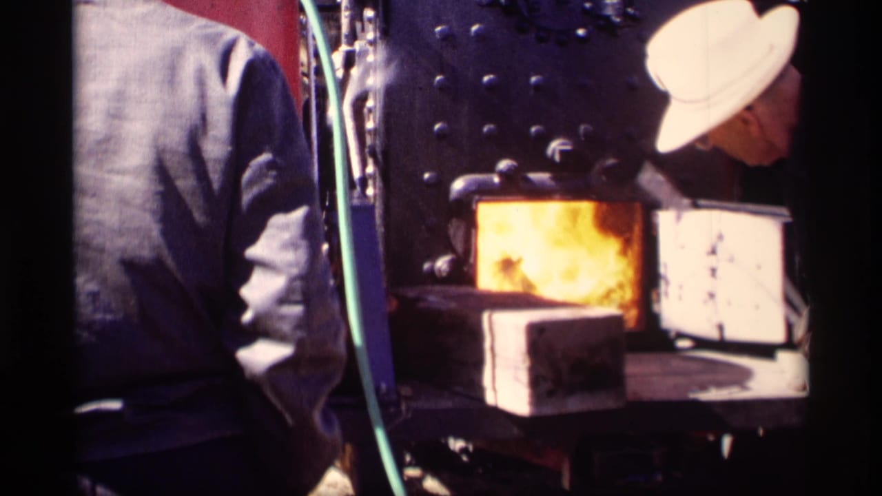 Close view of people beside a metal firebox with a bright flame and pale bricks nearby.