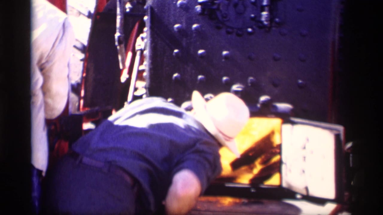 In Jordan, Minnesota in 1969, a worker bends toward a glowing steam train firebox beside dark riveted metal.