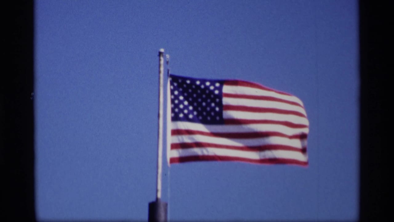 U.S. flag extended by wind beside a vertical flagpole.