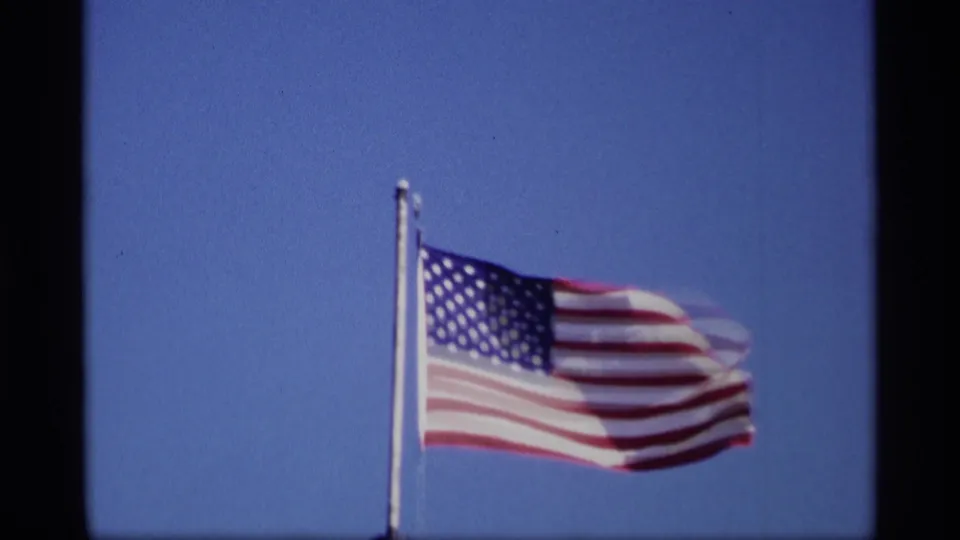 A closer 8mm view shows the U.S. flag rippling against blue sky in the 1969 Jordan, Minnesota clip.