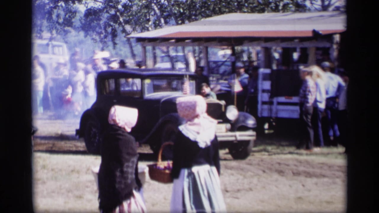 Black vintage car beside a pavilion as two bonneted women stand in the foreground.