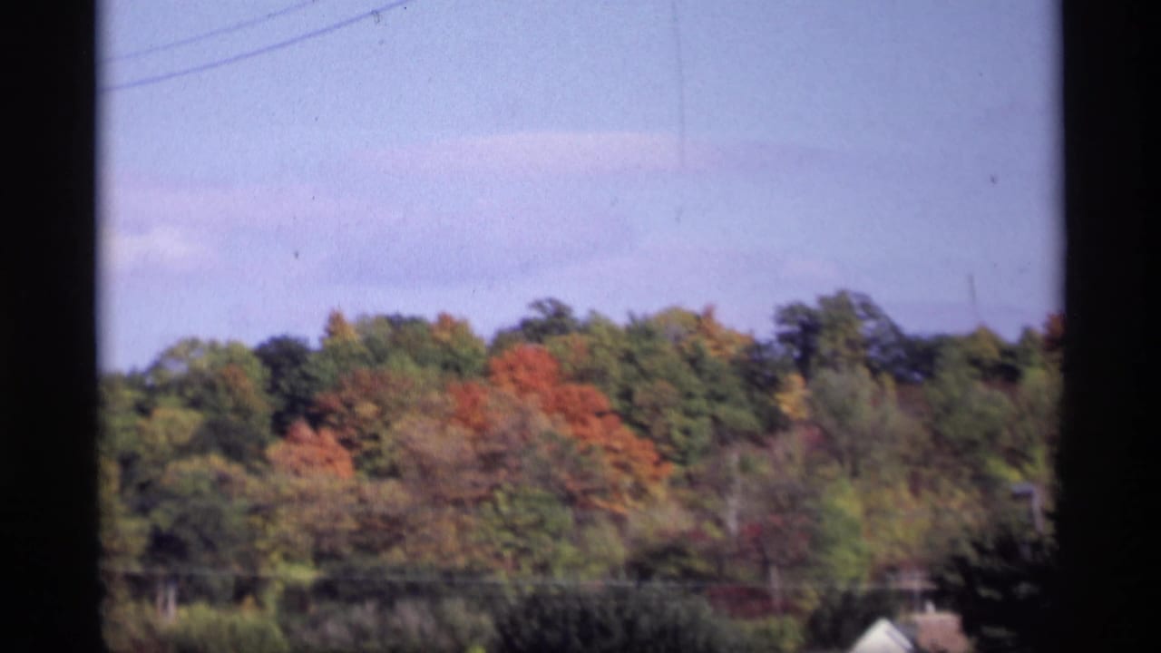 1969 Jordan, Minnesota home-movie frame showing a colorful autumn tree line and pale sky, softly focused with dark film borders.