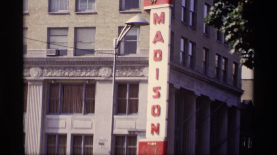 Street view of the Madison building facade with a tall red vertical sign, upper windows, and a streetlight.