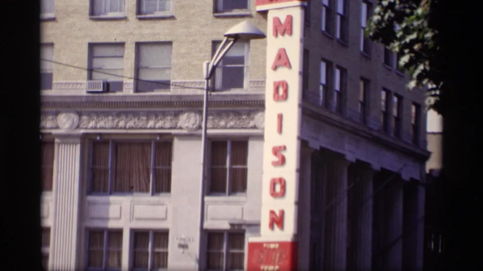 Closer 8mm view of the Madison building, showing the red sign, masonry facade, windows, and streetlight.