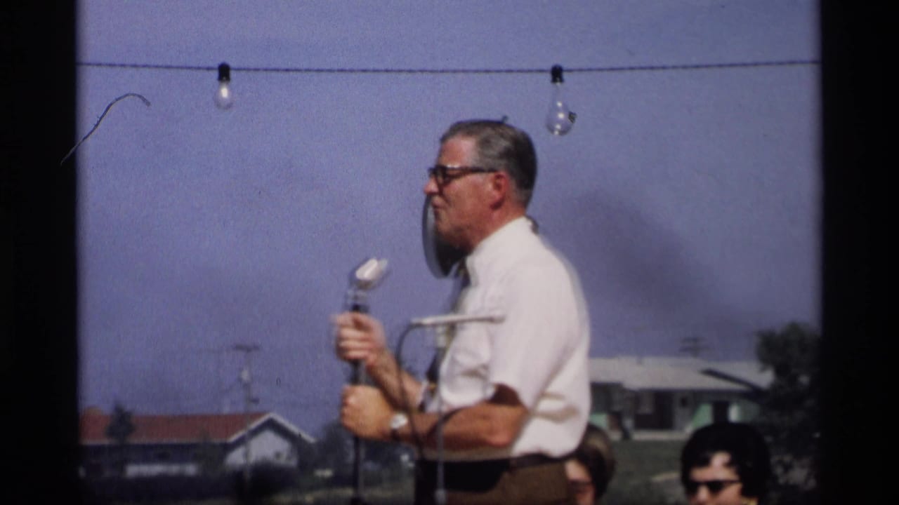 In Mabel, Minnesota, 1969, a man in a white shirt and tie appears to speak into a microphone at an outdoor gathering.