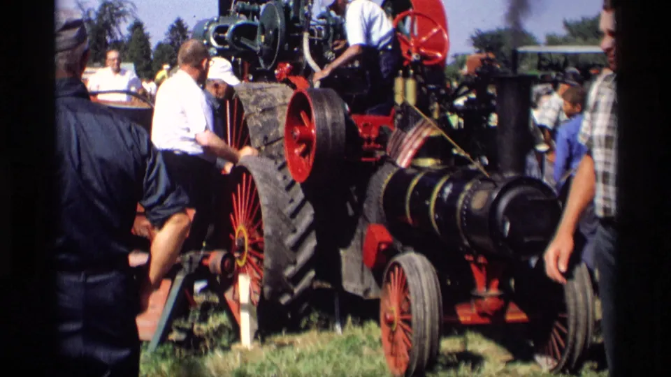 A close handheld view shows spectators and a demonstrator near the steam tractor machinery at the Mabel, Minnesota event.