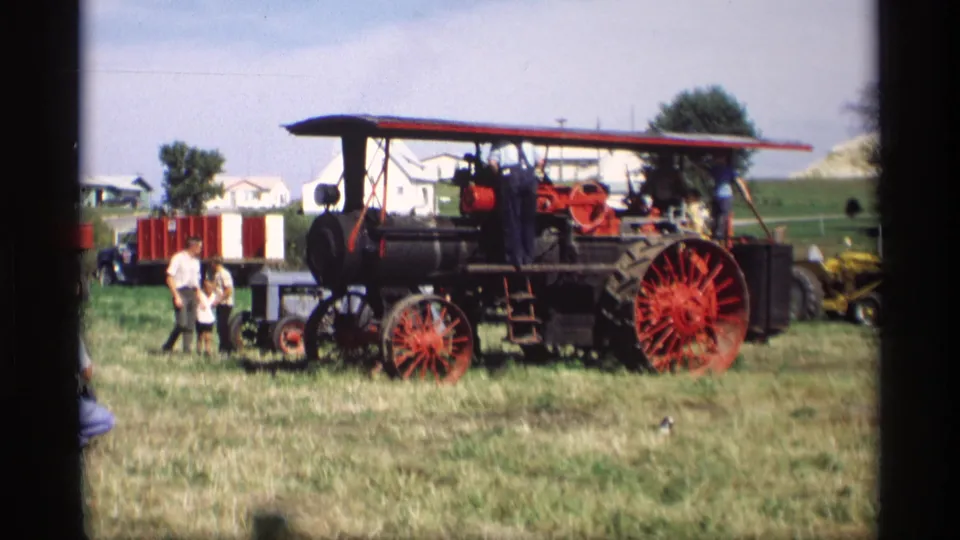 A wider view shows the steam tractor on a grassy fairground with people and houses in the background in Mabel, Minnesota, 1969.