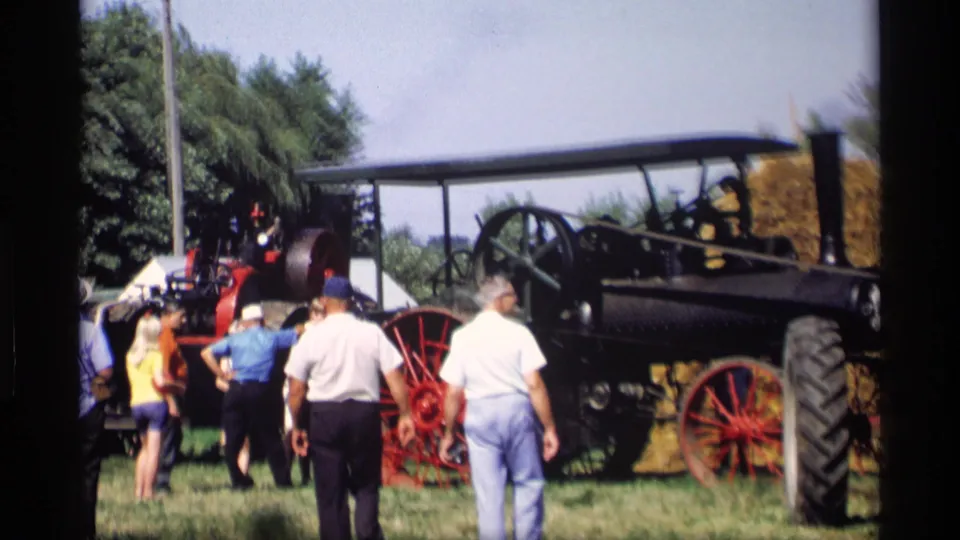 1969 Mabel, Minnesota frame showing attendees walking toward a steam tractor with red spoked wheels and a hay bale behind it.