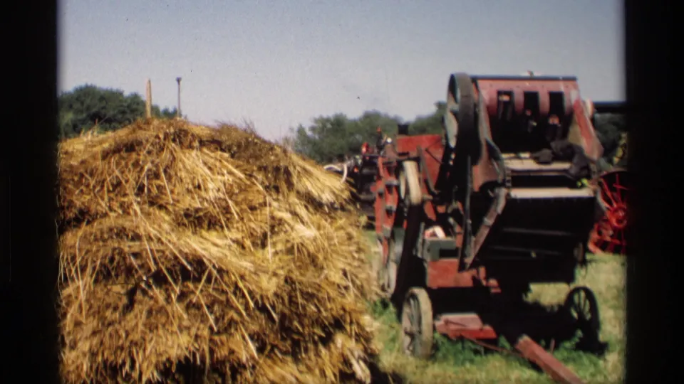 1969 Mabel, Minnesota 8mm frame showing a straw mound beside a red thresher or farm machine with small people nearby.
